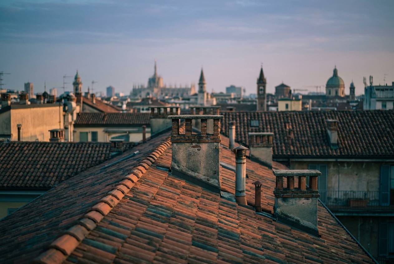 Immagine illustrativa: tetti in coppi di Milano al tramonto con skyline sfocato