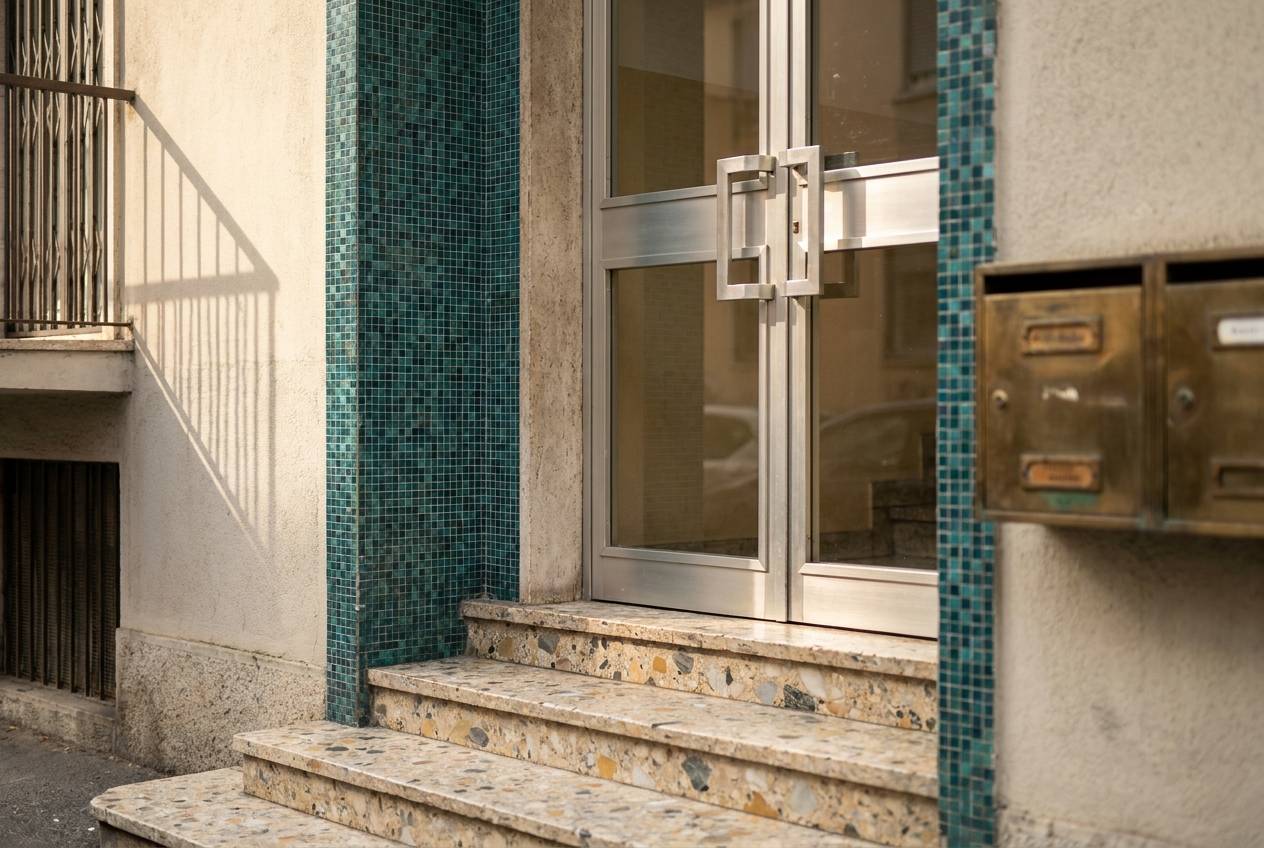 Immagine illustrativa: ingresso di palazzina anni '70 ad Affori con mosaico ceramico e portone in alluminio e vetro.