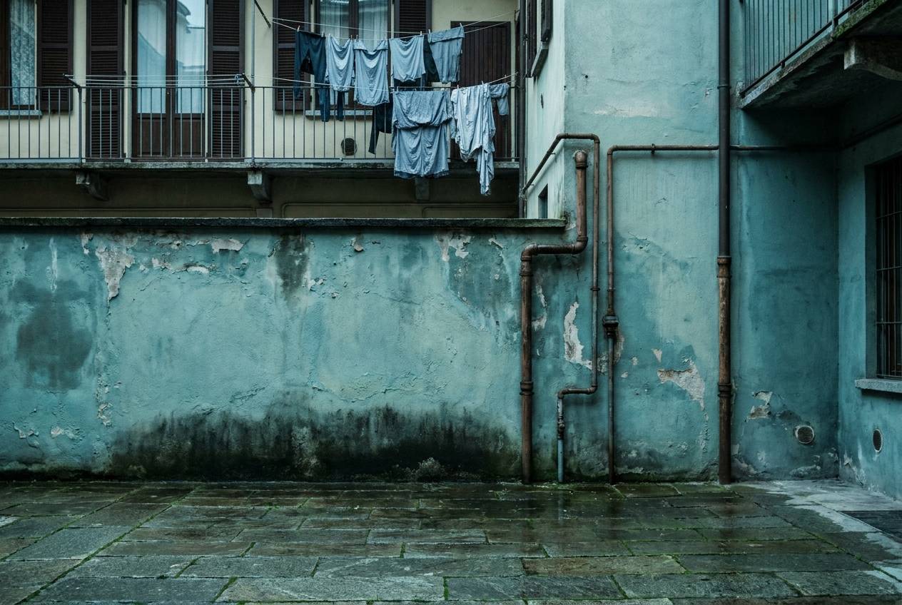 Immagine illustrativa: cortile di casa di ringhiera sui Navigli con umidità di risalita sul muro e vecchie tubazioni a vista.