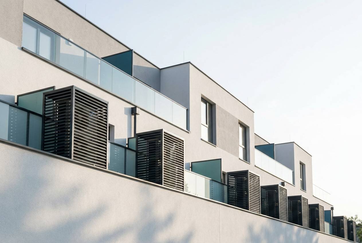 Immagine illustrativa: facciata di un edificio recente con unità esterne di pompe di calore nei vani schermati dei balconi.